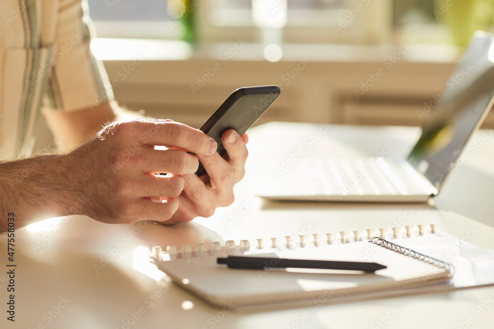 Horizontal close-up shot of unrecognizable man sitting at desk in modern office surfing Internet on smartphone Horizontal close-up shot of unrecognizable man sitting at desk in modern office surfing Internet on smartphone