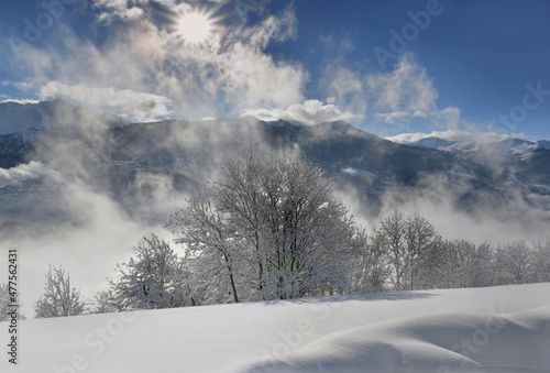 white mountain landscape  covered with snow  in front of cloudy sky  illuminated by the sun © coco