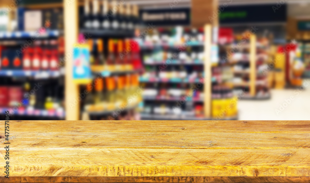 Empty wood table top on blurred market racks with bottles of alcoholic beverages. Mock up for display of product.