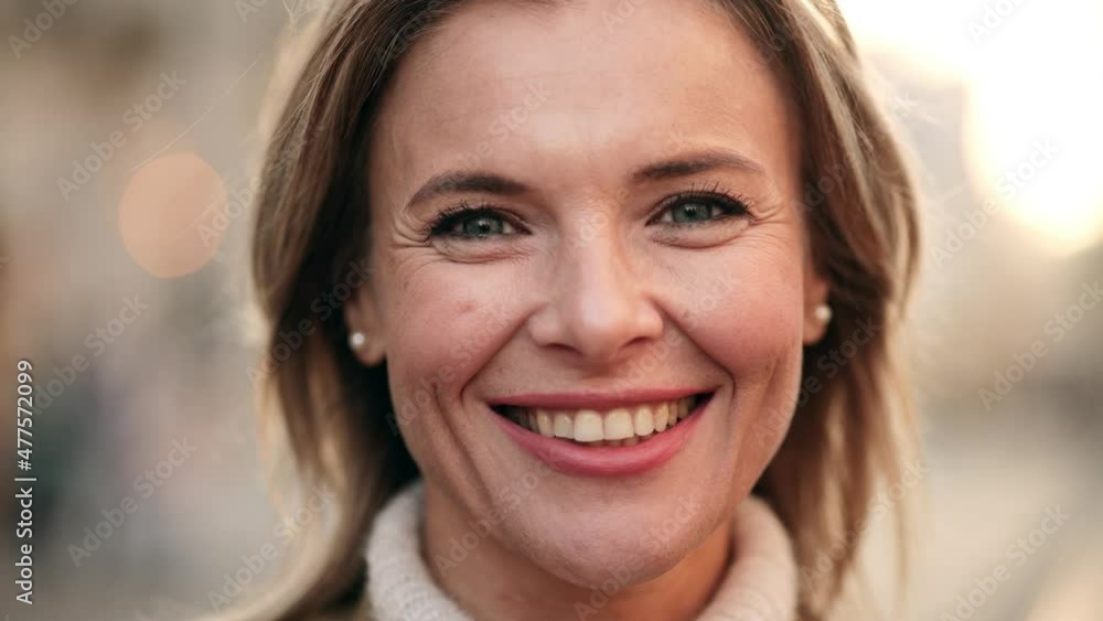 Lovely middle-aged blond woman with a beaming smile and looking at the camera. Happy adult woman smiling with teeth smile outdoors and stay on city street at sunset time Lovely middle-aged blond woman with a beaming smile and looking at the camera. Happy adult woman smiling with teeth smile outdoors and stay on city street at sunset time