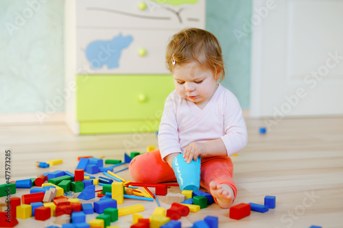 Cute little baby girl playing with educational toys. Happy healthy child having fun with colorful different wooden blocks at home or nursery. Baby crawling and learning colors and forms, indoors