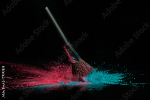 Blue and pink makeup powder brush fall on shiny black surface in a dust cloud