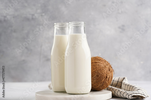 Two bottles with non-dairy milk and coconut on round marble board, grey background