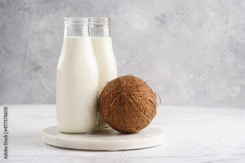 Two bottles with non-dairy milk and coconut on round marble board