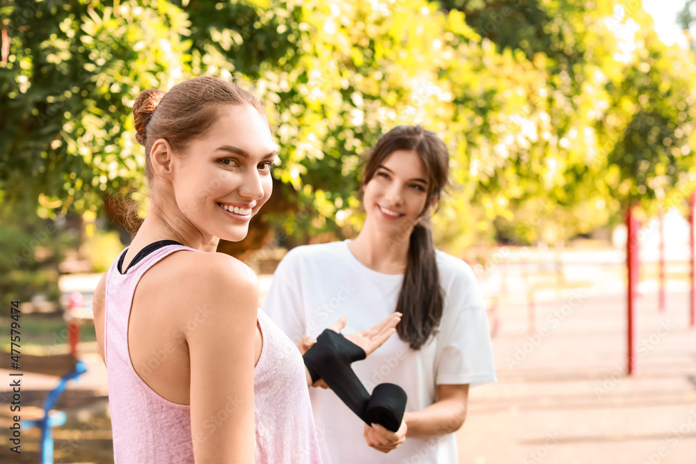 Sporty young woman bandaging her friend's hand on sport ground Sporty young woman bandaging her friend's hand on sport ground