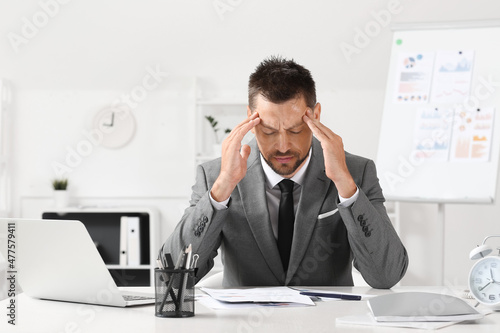 Tired young businessman sitting at table in office