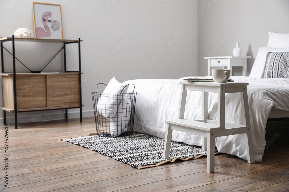 Obraz premium White step stool with cup and magazines near bed in modern room