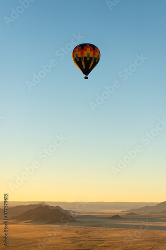 A vertical shot of a hot air balloon flying against a deep blue sky over the Sossusvlei landscape at sunrise, Namibia