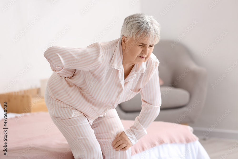 Senior woman suffering from back pain near bed at home Senior woman suffering from back pain near bed at home