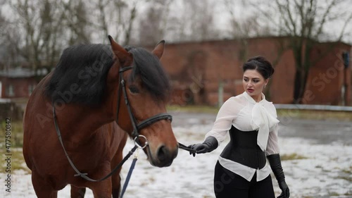 strict horsewoman is leading brown steed in horse yard in winter day photo