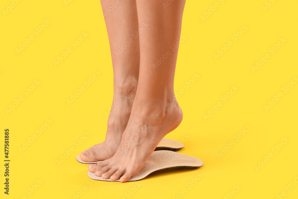 Female feet and orthopedic insoles on yellow background