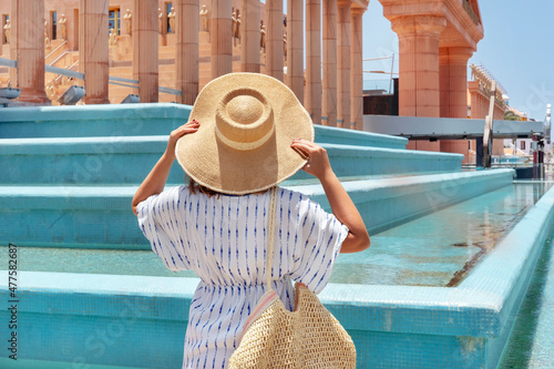 Fotografía Rear view of young woman holding a wide brimmed hat and facing towards the entra