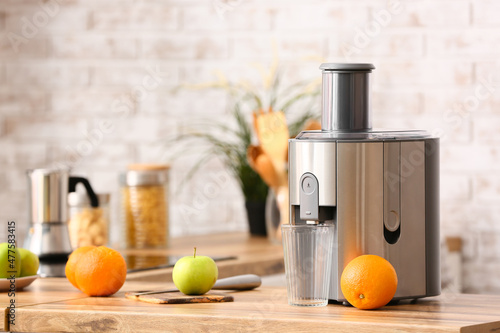 Modern juicer with fresh fruits on table in kitchen photo