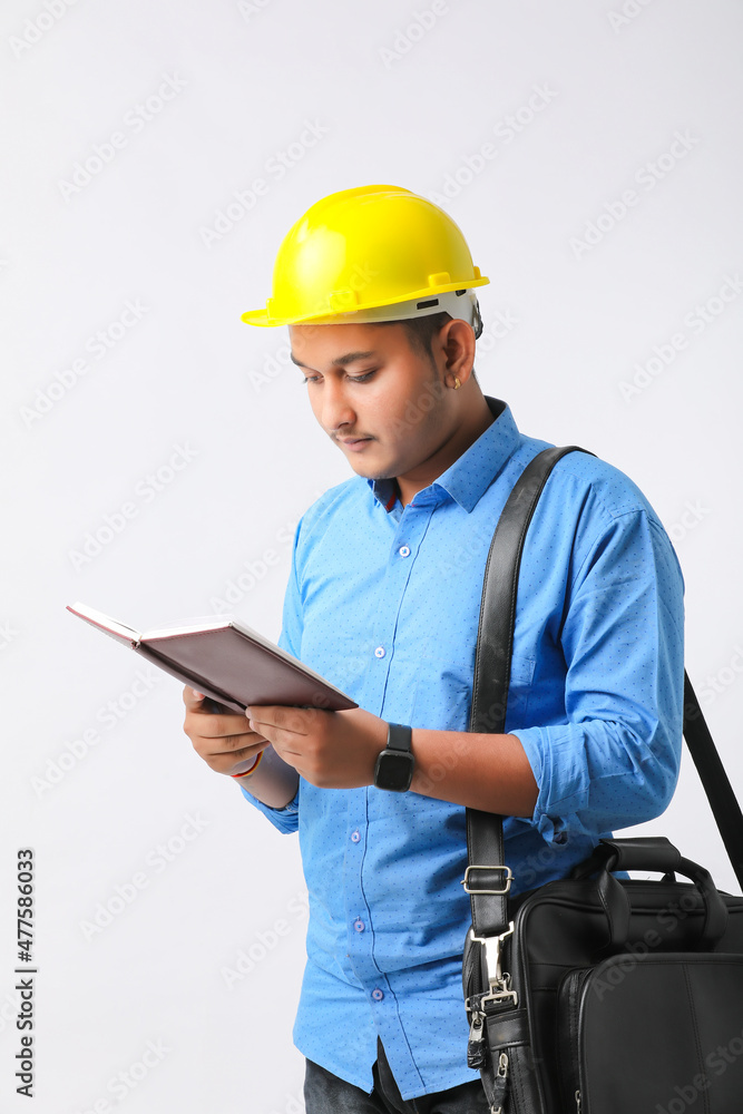 Young Indian engineer wearing yellow color hard hat and reading diary on white background Young Indian engineer wearing yellow color hard hat and reading diary on white background