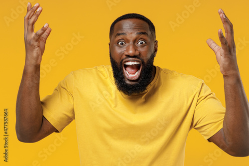 Young angry furious indignant stressed black man 20s wearing bright casual t-shirt spread hands screaming shout isolated on plain yellow color background studio portrait. People lifestyle concept