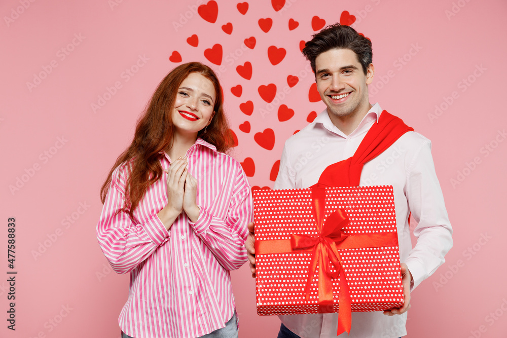 Young smiling couple two friends woman man 20s wearing casual shirt hold red present box with gift ribbon bow isolated on plain pastel pink background. Valentine's Day birthday holiday party concept.