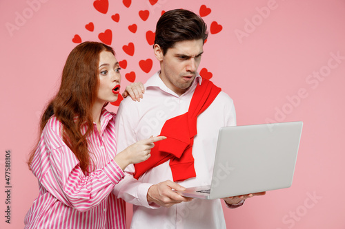 Young shocked couple two friends woman man in casual shirt hold use work on laptop pc computer isolated on plain pastel pink background studio portrait. Valentine's Day birthday holiday party concept.