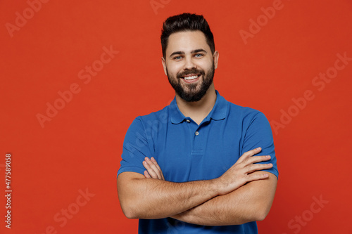 Young smiling cheerful fun cool happy caucasian attractive european man 20s in basic blue t-shirthld hands crossed folded isolated on plain orange background studio portrait. People lifestyle concept.