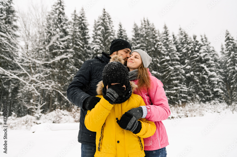 Happy family have fun in winter forest and looking at camera. Mother, father and son playing with snow. Family Christmas concept. Enjoying spending time together