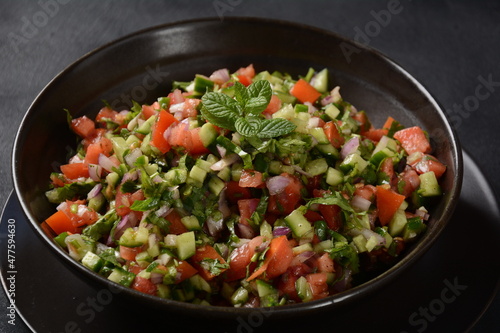 Shirazi Salad with tomatoes, cucumbers, red onions, parsley and mint with fresh lemon juice in a black bowl. Persian Shirazi vegetable salad closeup. Popular Israeli food