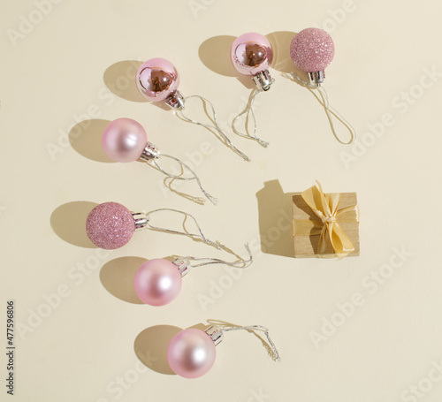 Shiny, pink Christmas baubles (balls) floating around a wrapped gift box on a beige background. Minimalist concept. Events and anniversaries. Newborn baby card template. Copy paste. Flat lay.