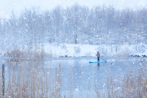 Winter SUP. Man rides on a supboard in snowfall on the river