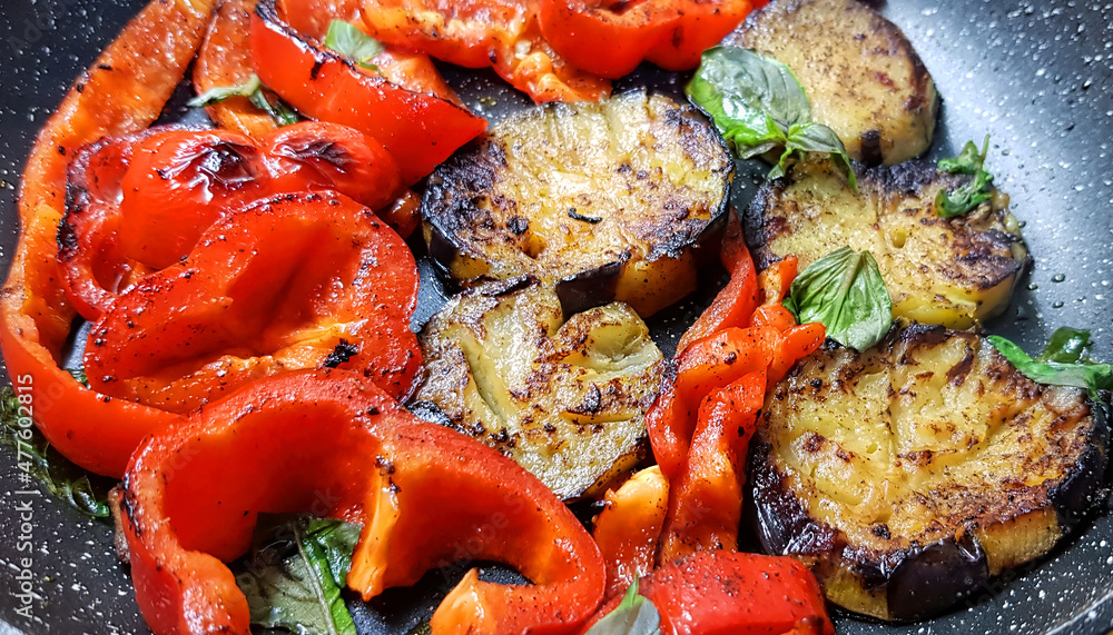 Fried sliced eggplants and sweet bell pepper with fresh basil leaves. Vegetable hot dish served in black frying pan. Healthy vegetarian food Fried sliced eggplants and sweet bell pepper with fresh basil leaves. Vegetable hot dish served in black frying pan. Healthy vegetarian food
