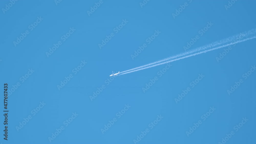 Distant passenger jet plane flying on high altitude on clear blue sky leaving white smoke trace of contrail behind. Air transportation concept Distant passenger jet plane flying on high altitude on clear blue sky leaving white smoke trace of contrail behind. Air transportation concept