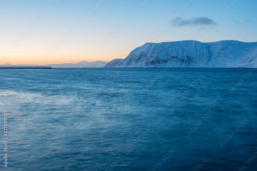 A tranquil horizontal seascape in winter with snow covered mountains in the background, after sunset, Norway