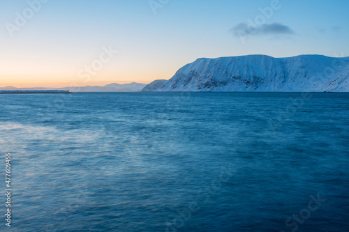 A tranquil horizontal seascape in winter with snow covered mountains in the background  after sunset  Norway