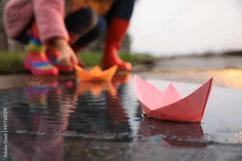 Foto Little girl and her mother playing near puddle outdoors, focus on paper boat