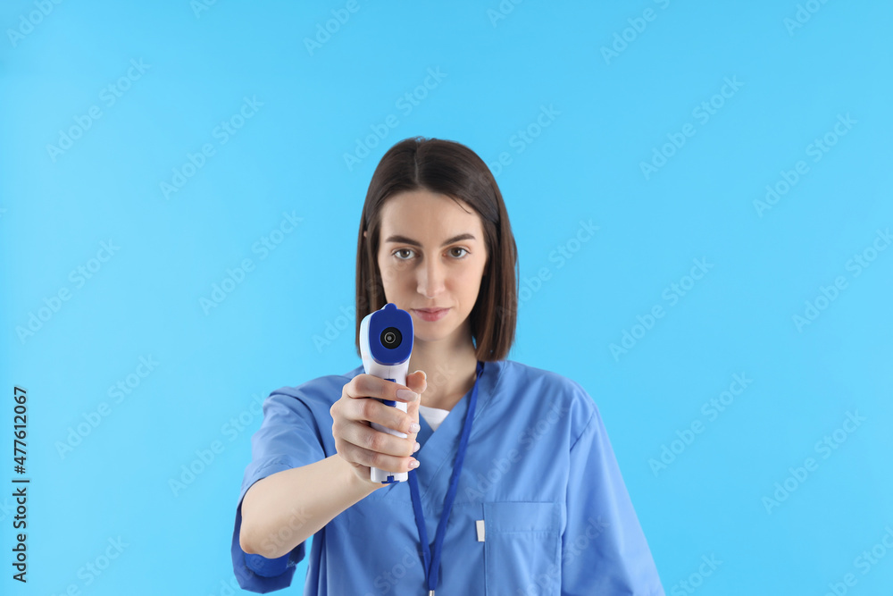 Female nurse with thermometer gun on blue background Female nurse with thermometer gun on blue background