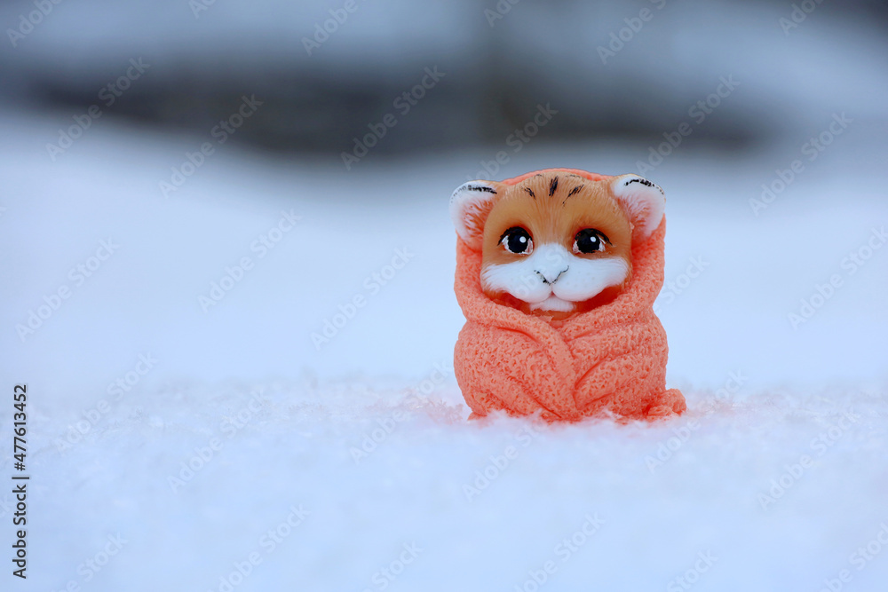 Fototapeta premium Tiger toy in snow on blurred forest background. Greeting card of New Year celebration, chinese 2022 year of the Tiger