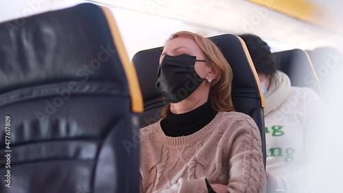 Young woman with face mask feeling unwell on plane, she is sitting with her eyes closed. Stress, headache, motion sickness and airsickness on plane during pandemic. photo