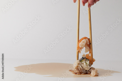 a hand and Chinese chopsticks holds a roll over other sushi, a portion of Asian food, rolls