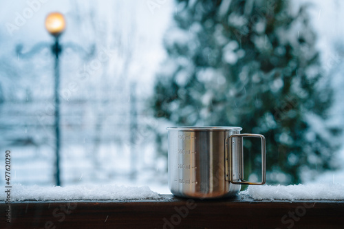Travel steel mug with coffee on snowy fence in a winter morning