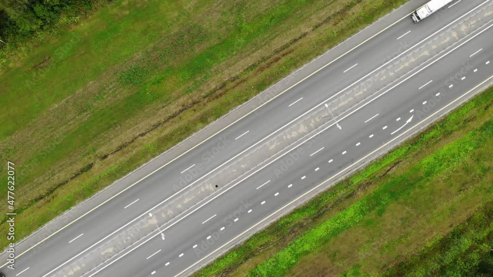 a straight section of the road by road high-speed highway. Summer and green grass. Trucks and cars. High quality 4k footage. Aerial drone view. Flying over. View top down. Drone moving sideways right a straight section of the road by road high-speed highway. Summer and green grass. Trucks and cars. High quality 4k footage. Aerial drone view. Flying over. View top down. Drone moving sideways right