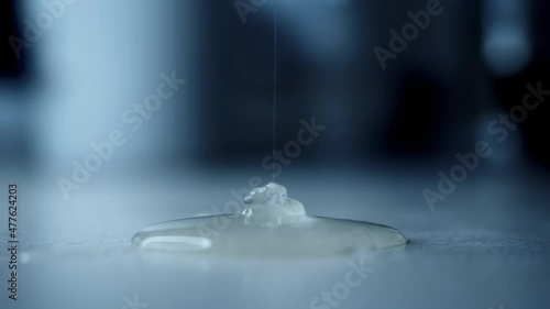 Thick liquid glue slowly pours in thin stream from above and spreads over surface. Liquid soap or dish gel dripping onto table. Close-up from side. Unknown dangerous chemical substance spills on floor