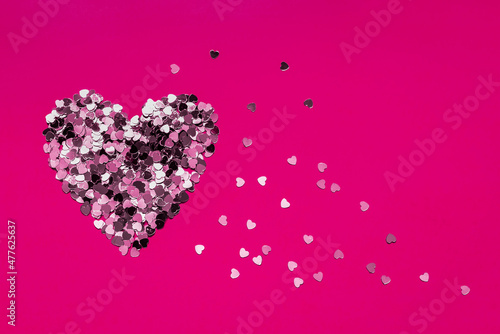 Valentine's Day heart made of confetti on a dark pink background. Copy space