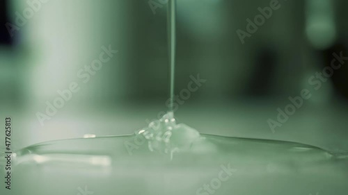 Liquid soap or dish gel dripping onto table. Thick liquid glue slowly pours in thin stream from above and spreads over surface. Close-up from side. Unknown dangerous chemical substance spills on floor