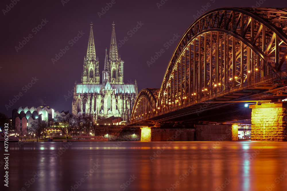 Obraz premium The illuminated Cologne Cathedral on the Rhine and the Hohenzollern Bridge in Cologne at night with purple sky.