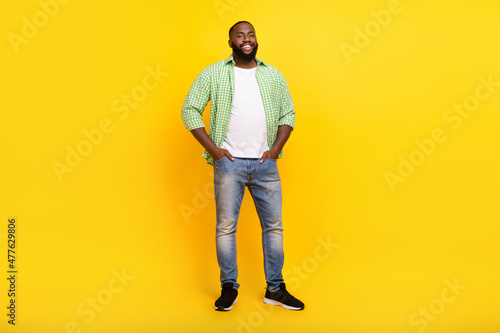 Full body photo of satisfied glad young person put arms in pockets toothy beaming smile isolated on yellow color background