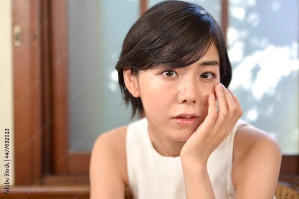 室内にて白いワンピース姿で微笑むショートヘアの清楚な女性