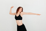 Curly redhead woman dancer training in the studio. Active young woman in casual summer outfit having fun indoor, looking to the side, stretching her arm