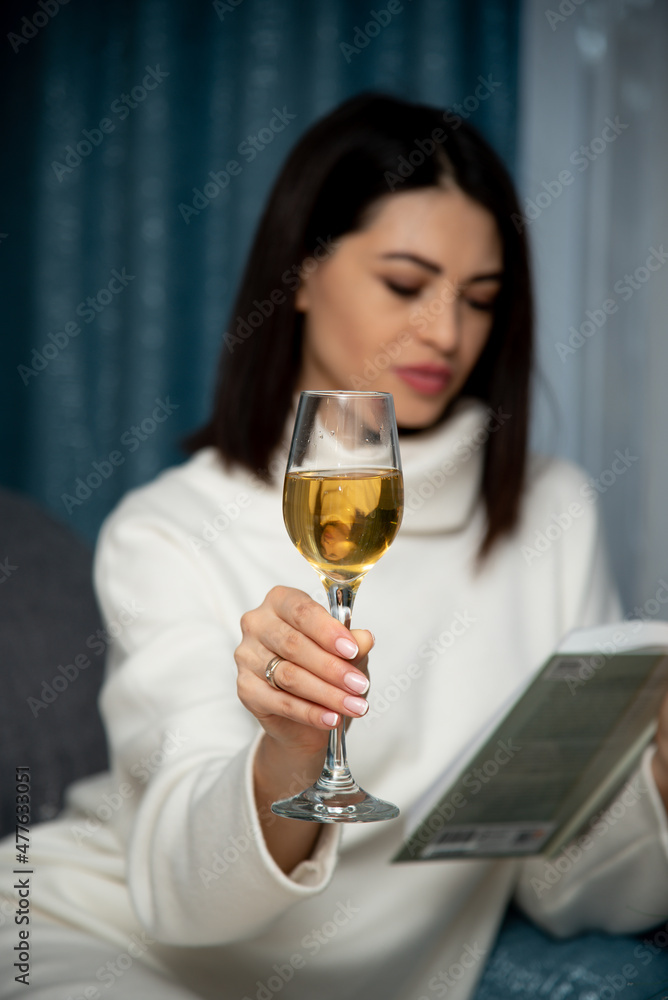 A beautiful young girl sits on the couch, drinks wine and reads a book. House. Relax.