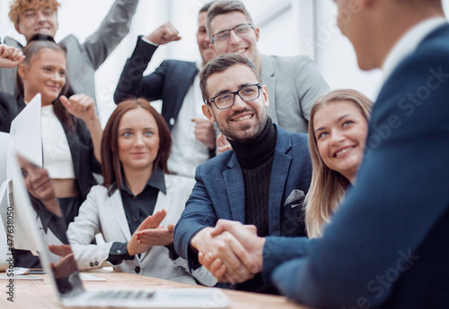 jubilant business team looking at the handshake of business partners