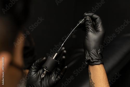 Tattooist assembling the sterilized needle in the grip. Wearing black gloves. Body art concept