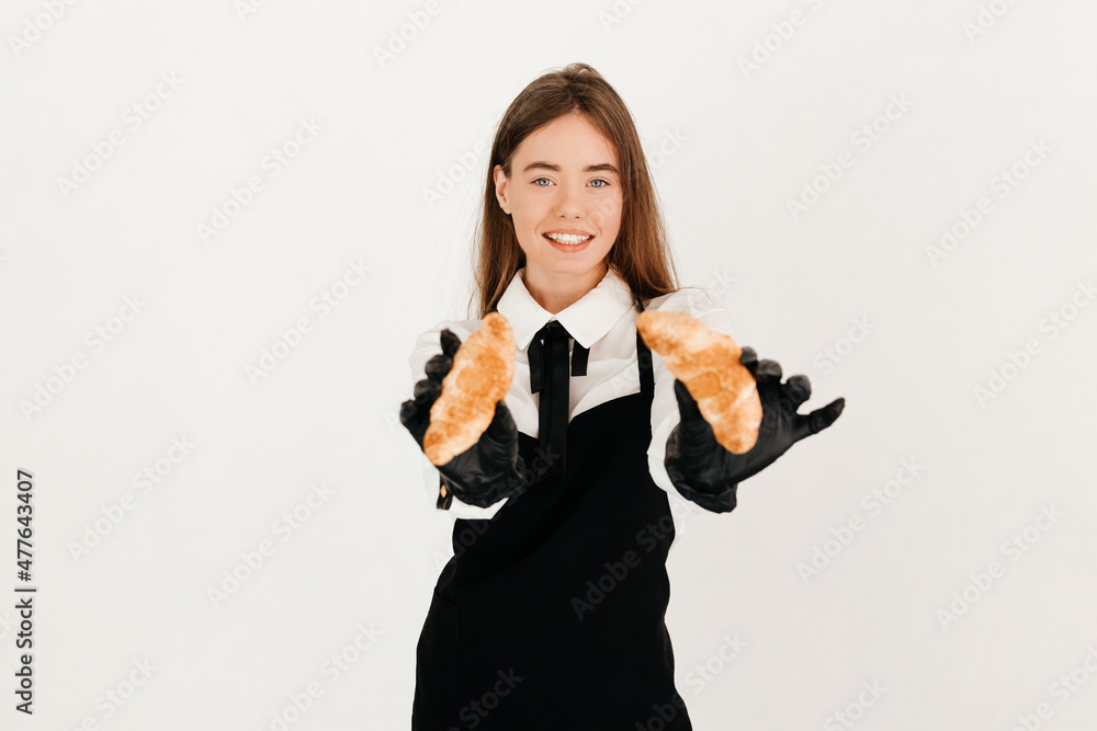 Pretty waitress in a uniform offering croissants to the camera, treating her favorite customers Pretty waitress in a uniform offering croissants to the camera, treating her favorite customers
