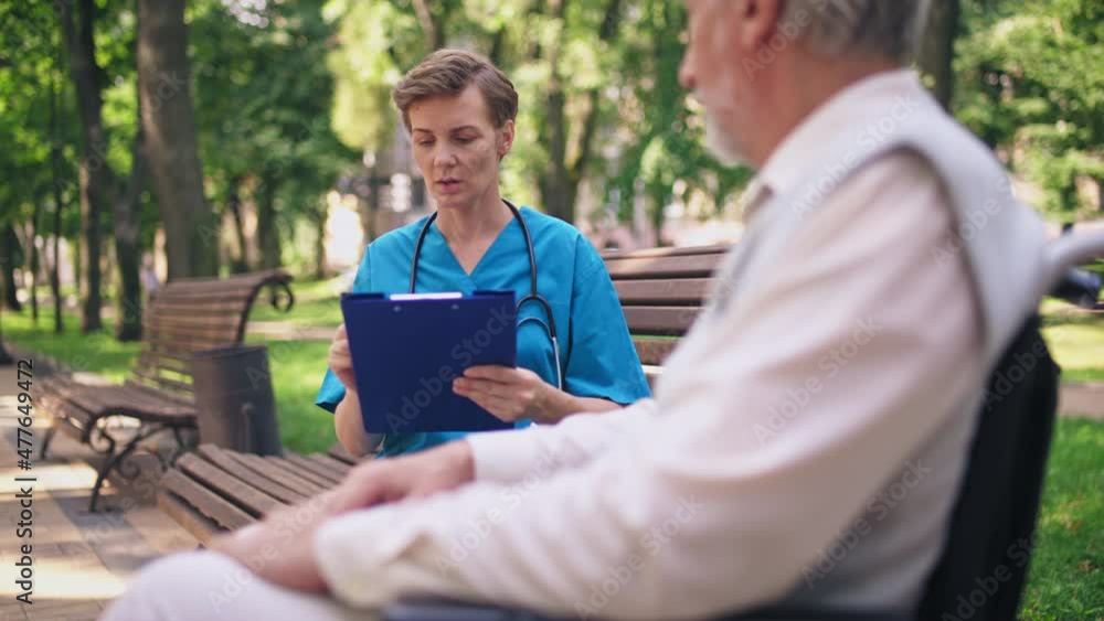 Physician writing in patient's card, talking to aged man in wheelchair, medicine Physician writing in patient's card, talking to aged man in wheelchair, medicine