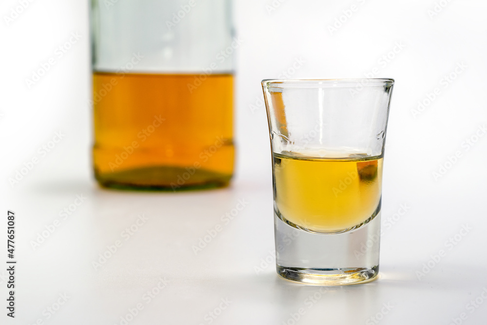 Alcoholic drink in a glass and bottle of brandy in the back on white table. Of strong alcoholic intoxication. The concept of alcohol dependence. Alcohol intoxication. Alcoholic drink in a glass and bottle of brandy in the back on white table. Of strong alcoholic intoxication. The concept of alcohol dependence. Alcohol intoxication.
